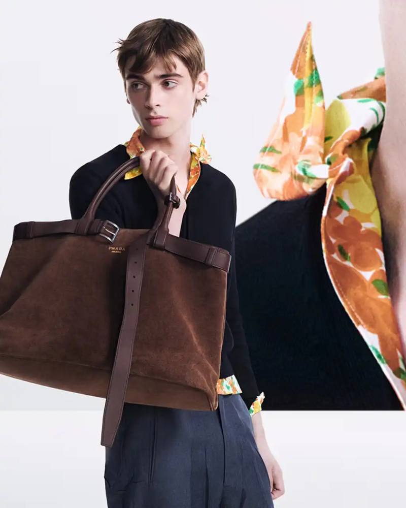 Prada Prada Spring/Summer 2025 campaign image showcasing models wearing the new collection, featuring belted tote bags in suede and leather, graphic t-shirts with Bernard Buffet artwork, and specialty eyewear with printed scenes on the lenses.