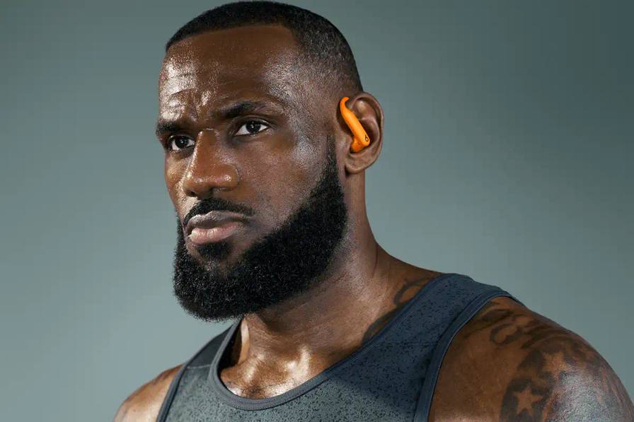 Lebron James wear Powerbeats Pro 2 wireless earphones in Electric Orange color, showing ear hooks and charging case with wireless charging capability.