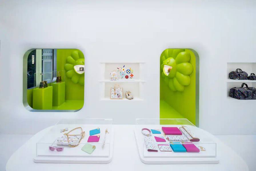 Brad Dickson Louis Vuitton's SoHo boutique exterior features Takashi Murakami's colorful flower motifs and rainbow monogram patterns. The multi-level space includes exhibition areas displaying archival pieces, a downstairs cinema, retail section with new collection items, and a themed café with custom-designed cups.