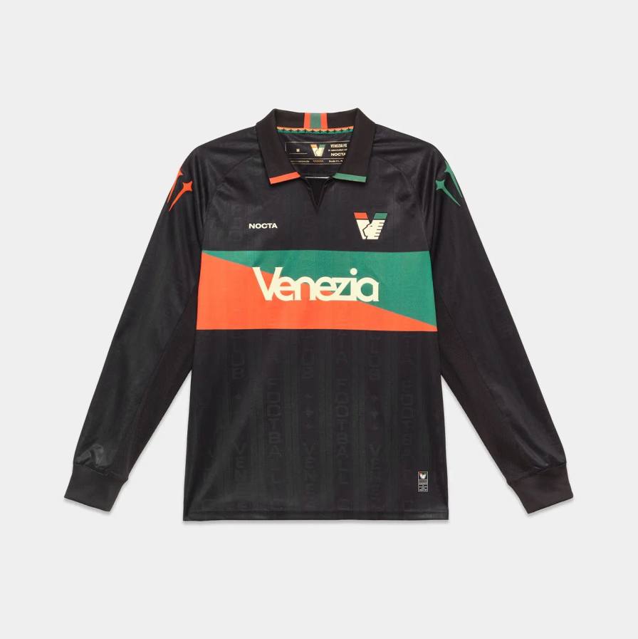 VENEZIA FC AND NOCTA RELEASE NEW HOME SHIRT An image of the Venezia FC home shirt from NOCTA showing black fabric with orange and green stripes, a polo collar, and black shorts.