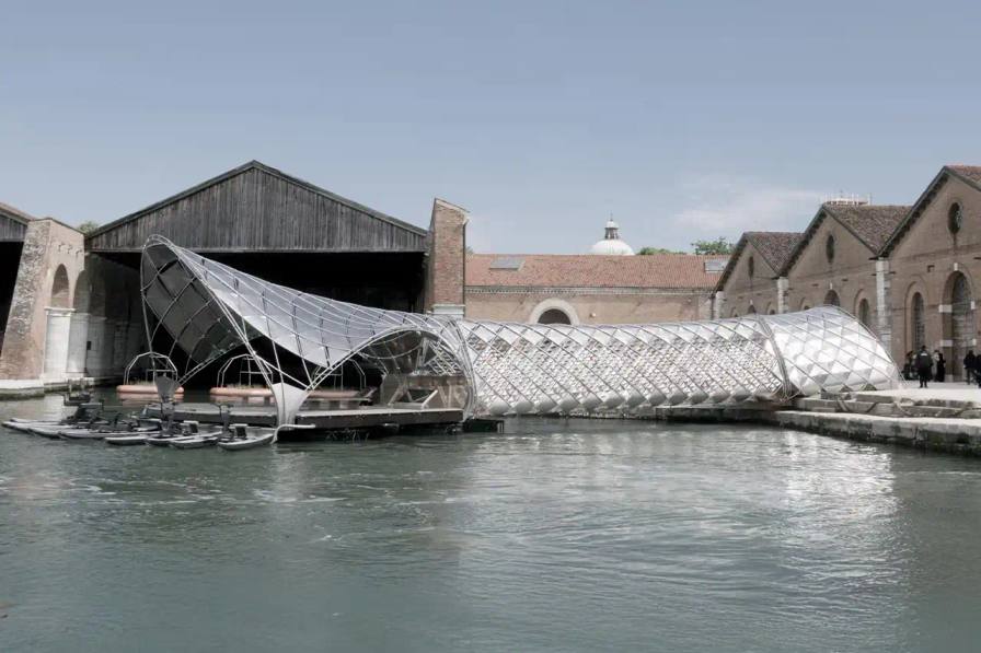 image about architectural partnership between Porsche and Norman Foster Foundation presenting electric mobility concepts at Venice Biennale. Content includes details about a 120-foot installation featuring sustainable transportation solutions like electric boats and water bikes, exhibition locations, and future collaboration plans. Text is structured with clear headings, bullet point summary, and descriptive paragraphs suitable for screen readers.