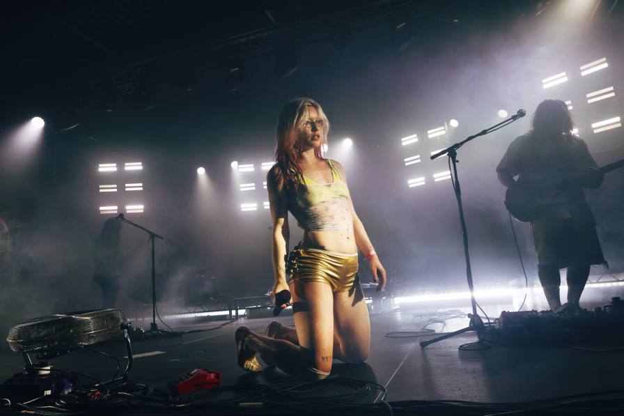WET LEG'S RHIAN TEASDALE SILENCES ONLINE NOISE IN BERLIN press photo of Wet Leg frontwoman Rhian Teasdale and an embedded 60-second manifesto film in which she navigates animated symbols representing online noise, opinions, and unsolicited advice before taking control of a car's steering wheel. A concert photo from the exclusive Berlin event, where Wet Leg headlined a live show tied to the campaign, is also referenced.