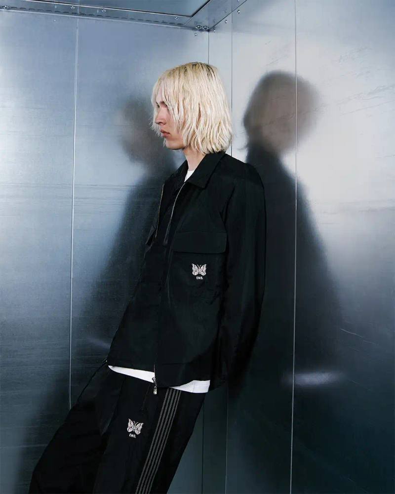 image about British retailer END.'s collaboration with Japanese streetwear brand Needles for their 20th anniversary. The partnership produced a five-piece collection made from crinkled nylon, including track pants, crew neck shirt, cabana shirt, sports jacket, and workers cap. All items feature platinum silver details and co-branded logos. The collection launched June 23rd, 2025, available online and in END. stores across the UK and Milan.