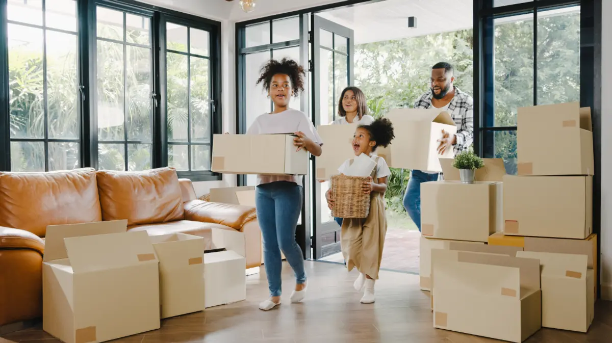 A family carrying moving boxes into a bright, modern home on moving day.