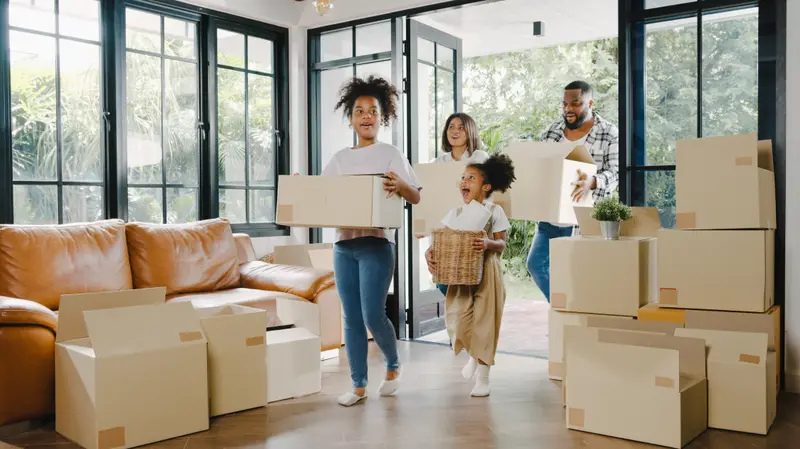 A family carrying moving boxes into a bright, modern home on moving day.