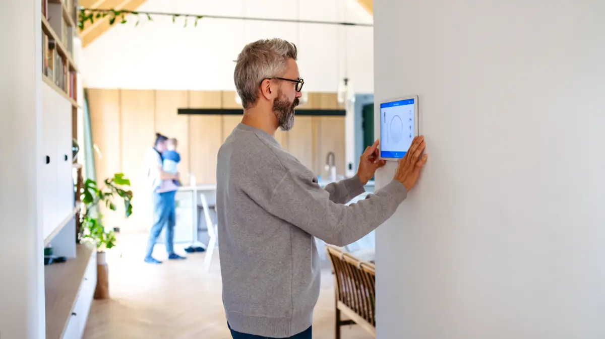 A man adjusting a smart home control panel mounted on the wall of a modern, open-plan home.