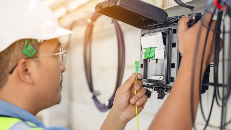 A technician connecting a fiber optic cable to a fiber distribution box during a home internet installation.