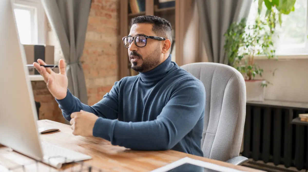 A man speaking on a video call at his desk in a home office