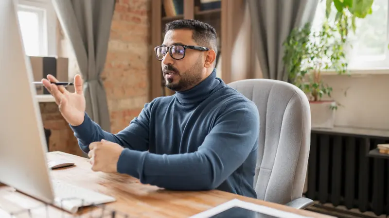 A man speaking on a video call at his desk in a home office