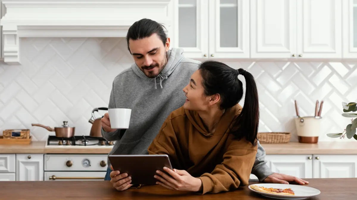 A couple looking at a tablet together over breakfast in a bright, modern kitchen.