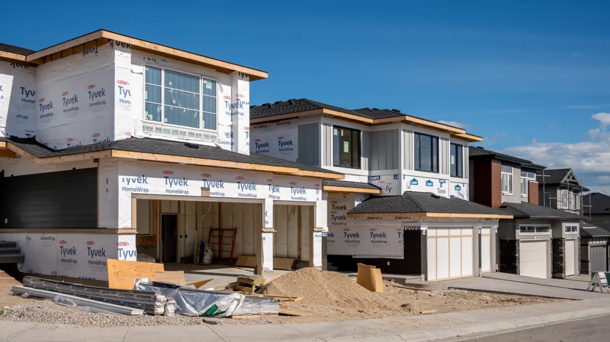 A row of new construction homes under various stages of completion in a residential development on a clear day.