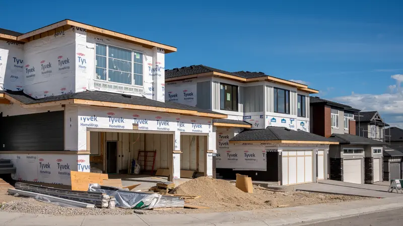 A row of new construction homes under various stages of completion in a residential development on a clear day.