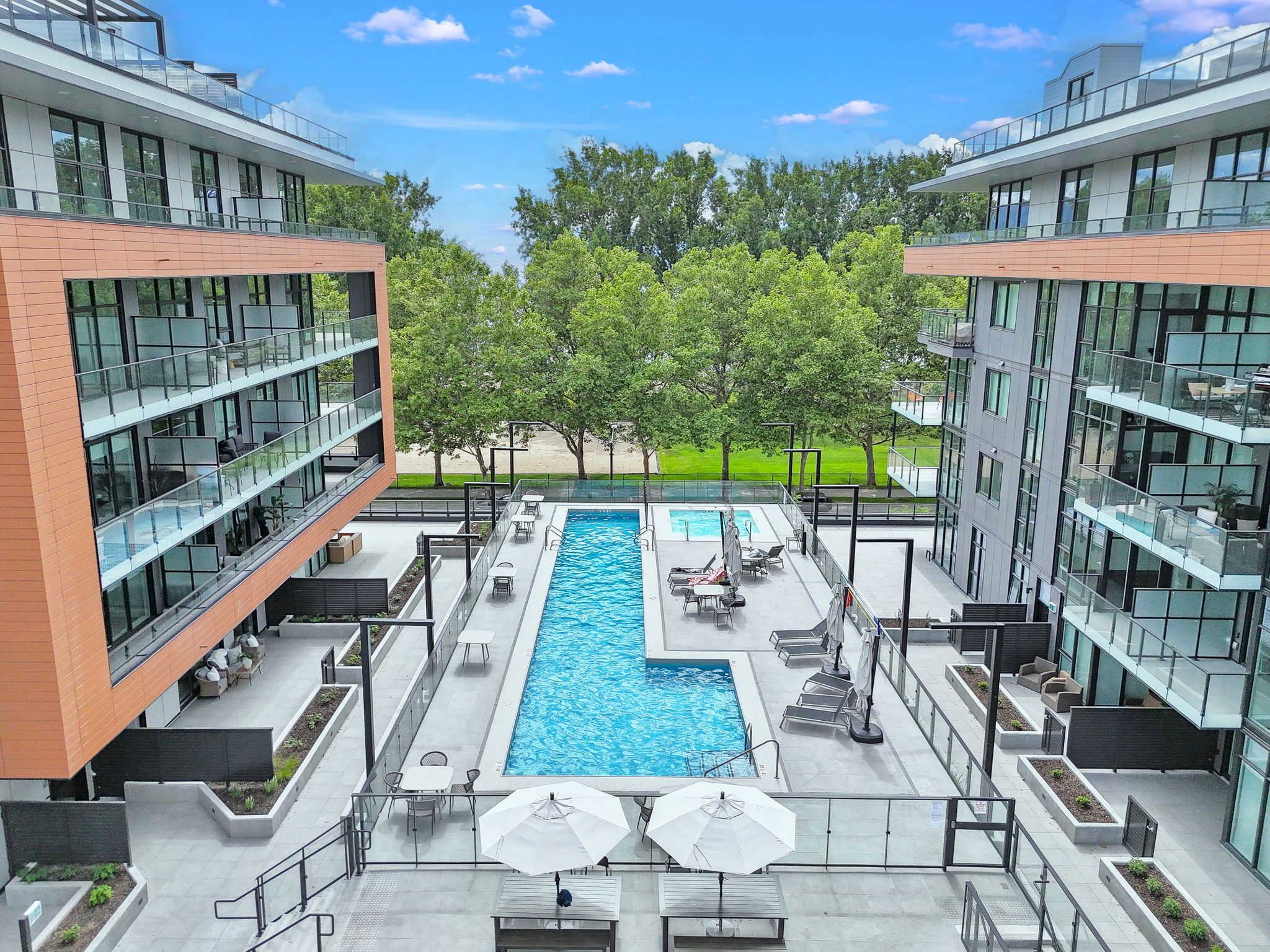 Long blue amenity pool looking across at a lush park space on sunny day