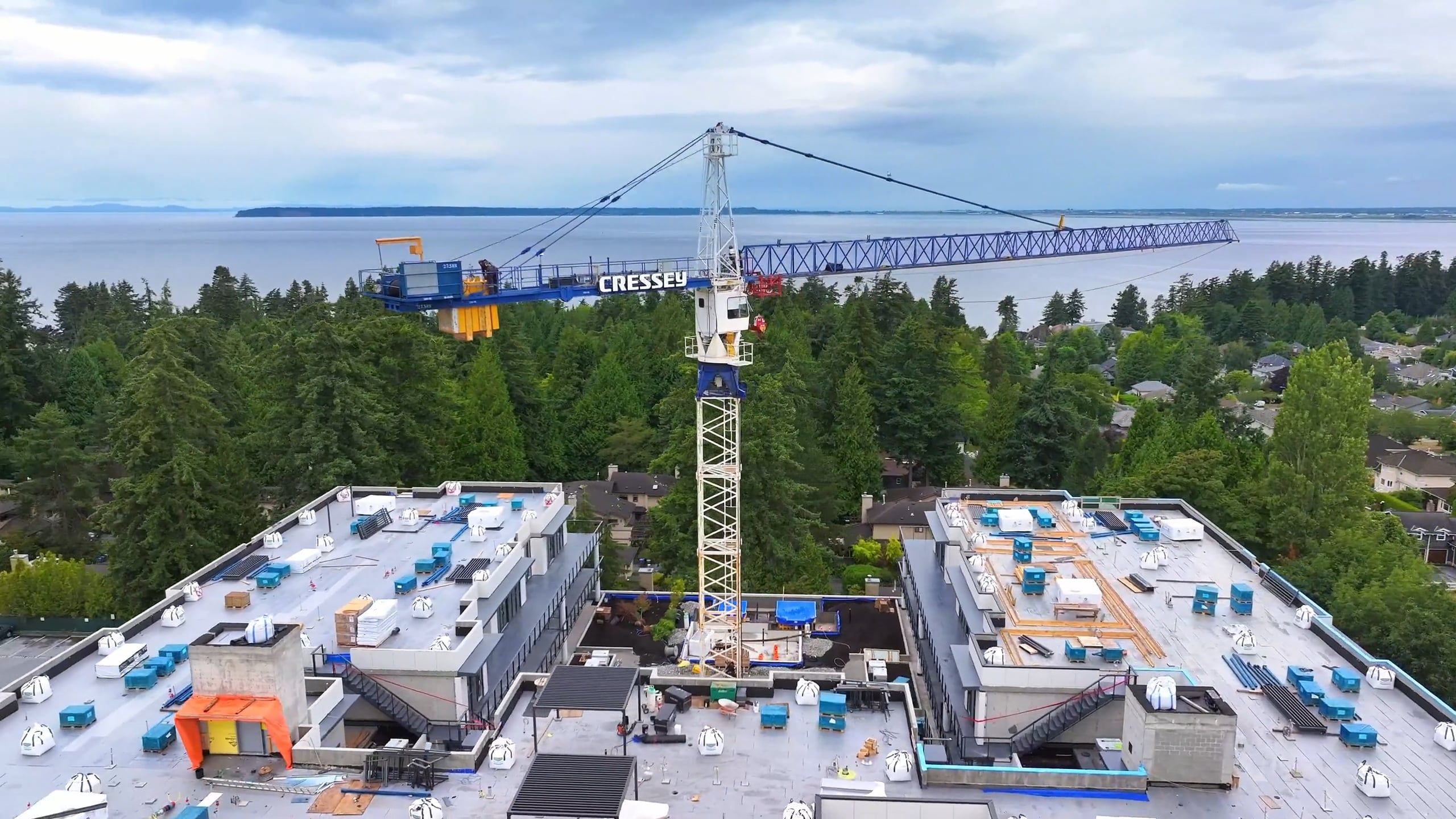Construction crane above building rooftop with view of trees and ocean on cloudy day