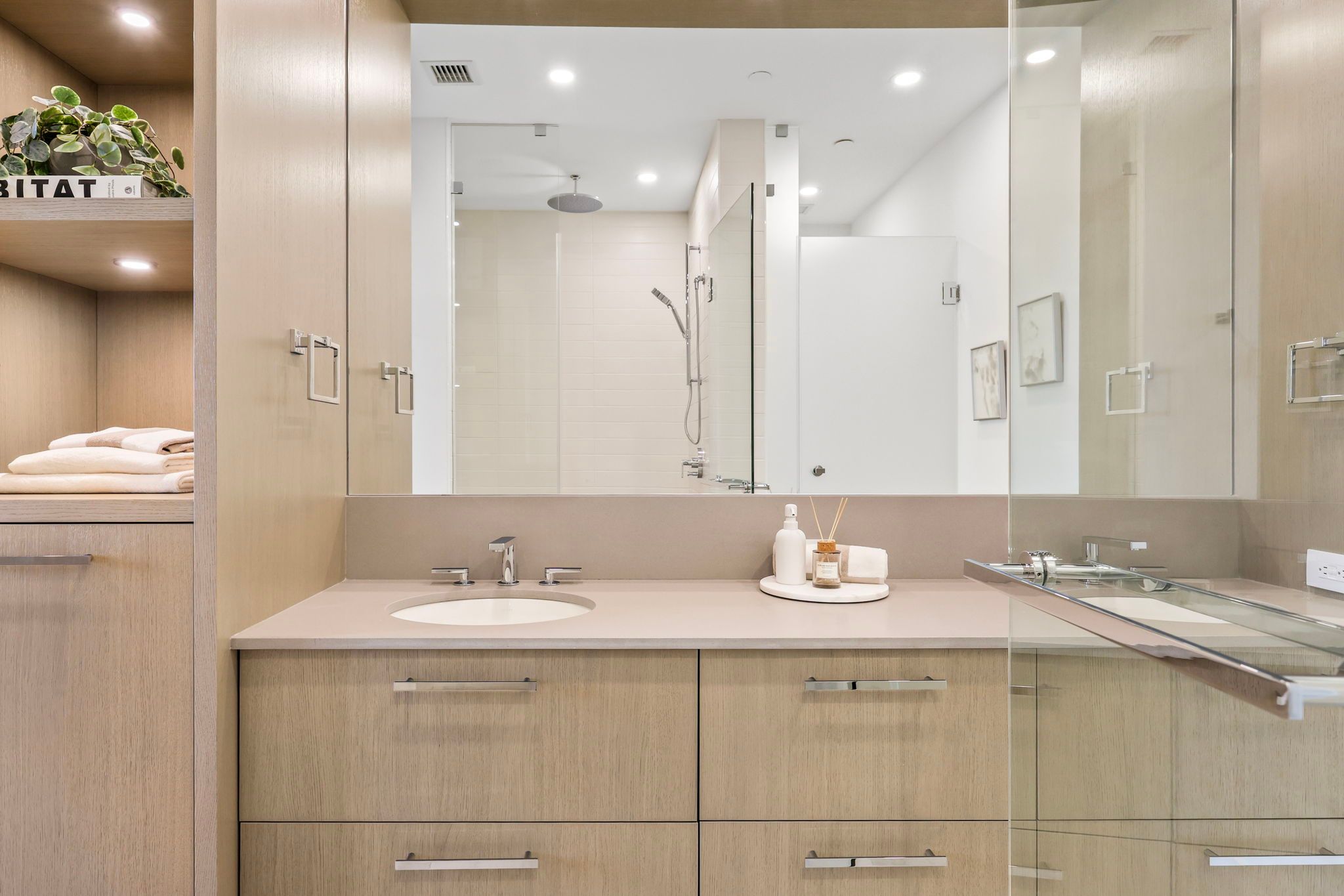 Bathroom with dual vanity, large mirror, light wood-tone cabinetry and glass shower