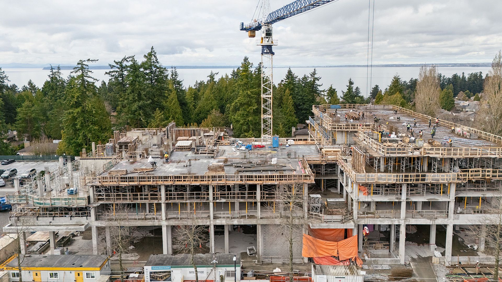 Concrete construction of residential building with trees and water behind on cloudy day