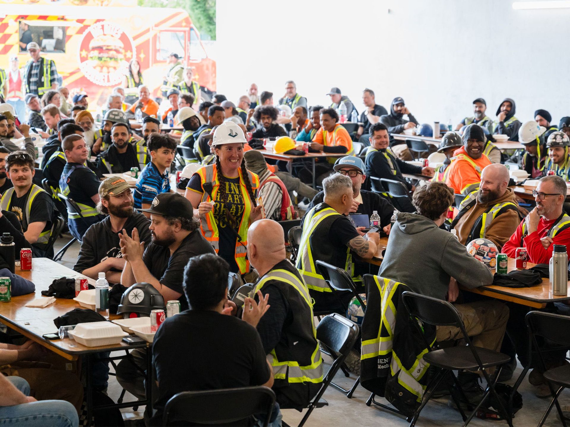 Construction team seated at celebration lunch; woman walking through crowd to claim prize