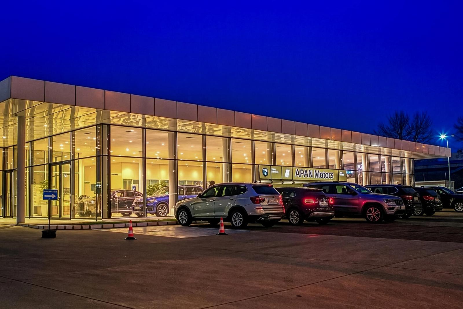  Showroom APAN Motors la blue hour — fațadă de sticlă cu mașini premium parcate în față