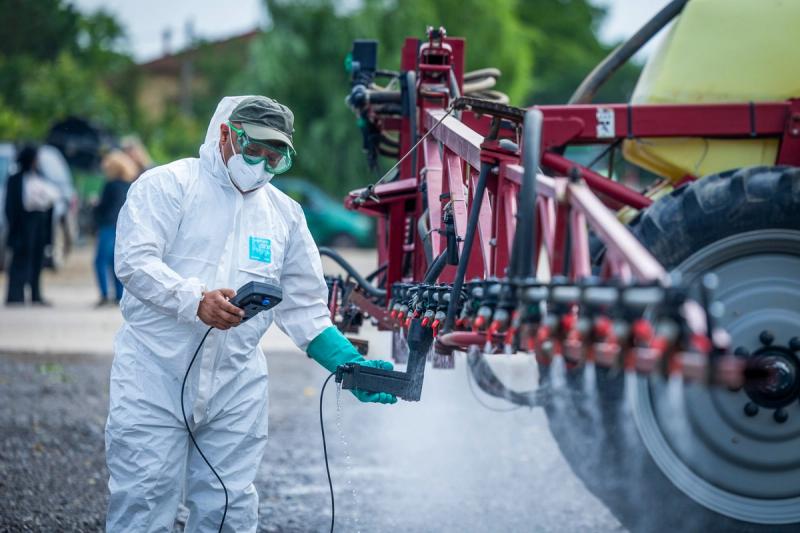 Inspector ANF în echipament de protecție verifică tehnic un utilaj agricol de stropit — control de etanșeitate, debit și uniformitate a duzelor.