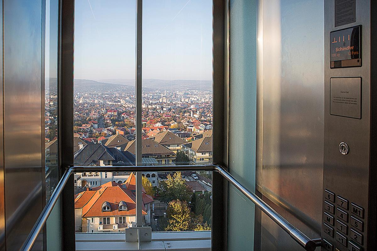 Liftul de sticlă al Grand Hotel Italia, cu vedere panoramică spre Cluj-Napoca și dealurile din nord-vest, în lumină de toamnă.