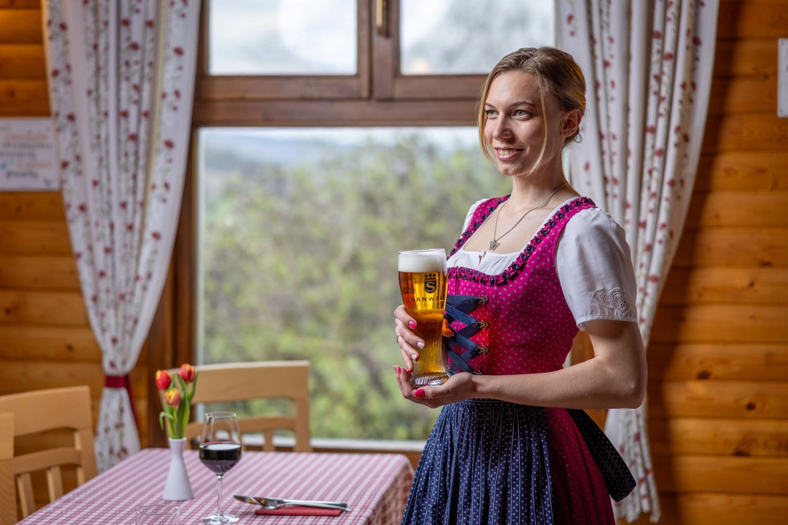 Chelneriță în dirndl tradițional bavarez servind bere wheat — interior cu vedere spre dealul împădurit, Schwabenhof.