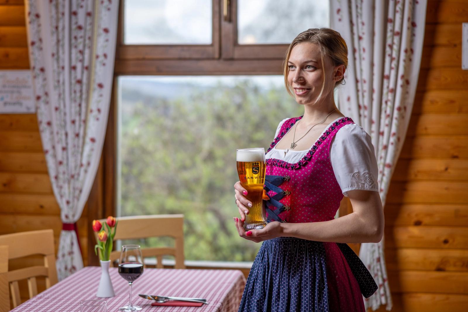 Chelneriță în dirndl tradițional bavarez servind bere wheat — interior cu vedere spre dealul împădurit, Schwabenhof.