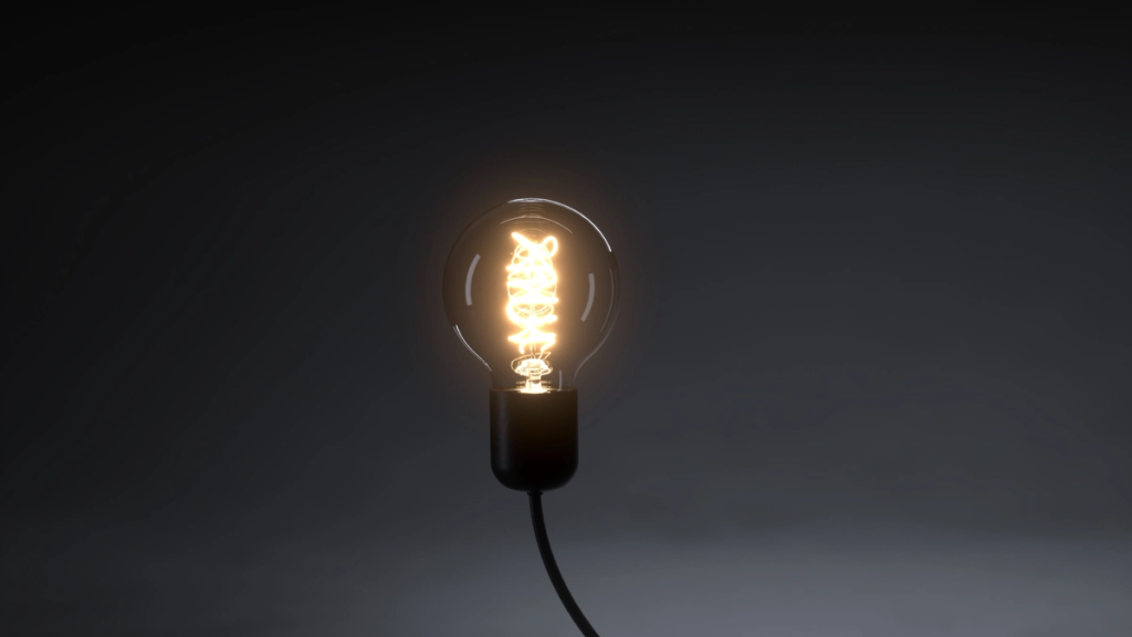 A glowing light bulb with a visible filament against a dark, minimalist background.