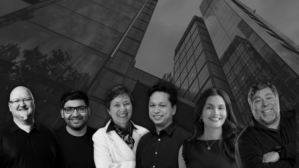 Six people smiling in front of a modern glass building backdrop, depicted in black and white.