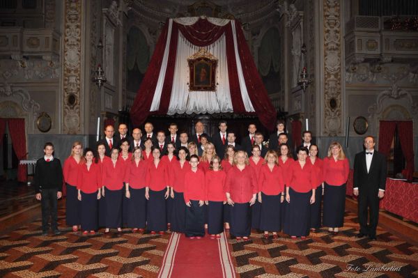 Foto di gruppo davanti all’altare addobbato con drappi rossi e bianchi: le donne in camicia rossa e gonna blu, dietro gli uomini in cravatta rossa