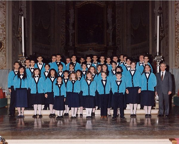 Foto di gruppo sui gradini dell’altare: ragazze e ragazzi in golfino turchese e papillon nero, le ragazze in gonna blu; a destra un uomo in grigio