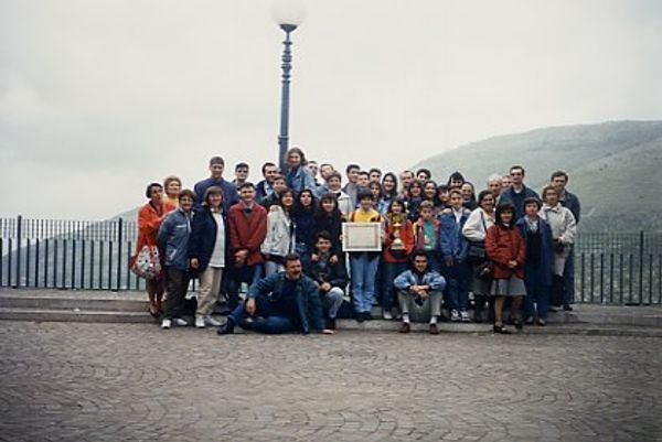 Foto di gruppo su un belvedere lastricato con la ringhiera e i monti nella foschia; al centro i ragazzi mostrano un diploma incorniciato e una coppa