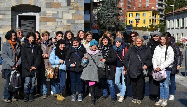 Una ventina di donne e ragazze in cappotto e sciarpa, in posa per strada davanti a un edificio di pietra; una bambina fa il segno della vittoria