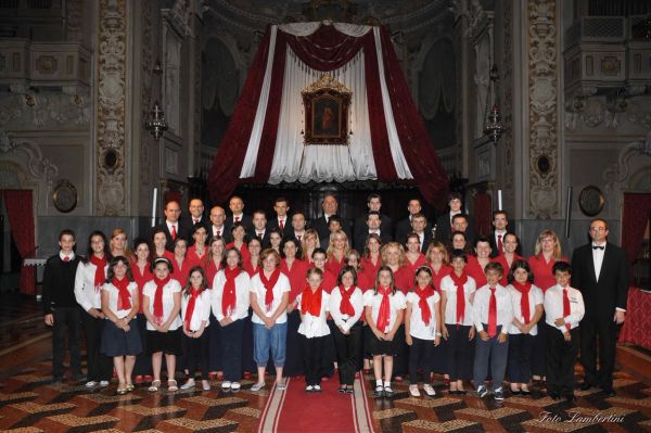 Davanti all’altare, in prima fila bambini e ragazzi in camicia bianca e foulard rosso, dietro le donne in rosso e gli uomini in giacca scura