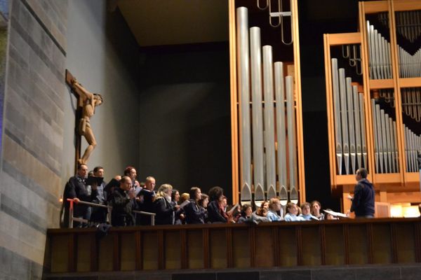Prova sul palco rialzato accanto alle grandi canne dell’organo: il coro, in abiti di tutti i giorni, canta sotto un crocifisso di legno