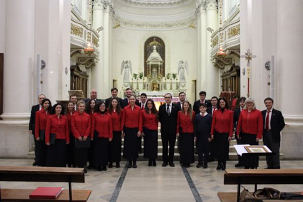 Foto di gruppo in una chiesa luminosa dalle colonne bianche: le donne in giacca rossa, gli uomini in abito scuro; sullo sfondo l’altare tra due angeli