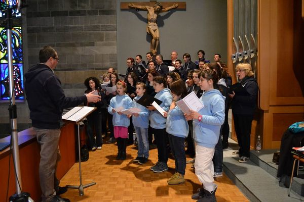 Prova in chiesa sotto un grande crocifisso di legno: un uomo in felpa dirige al leggio, davanti i bambini in felpa azzurra, dietro gli adulti
