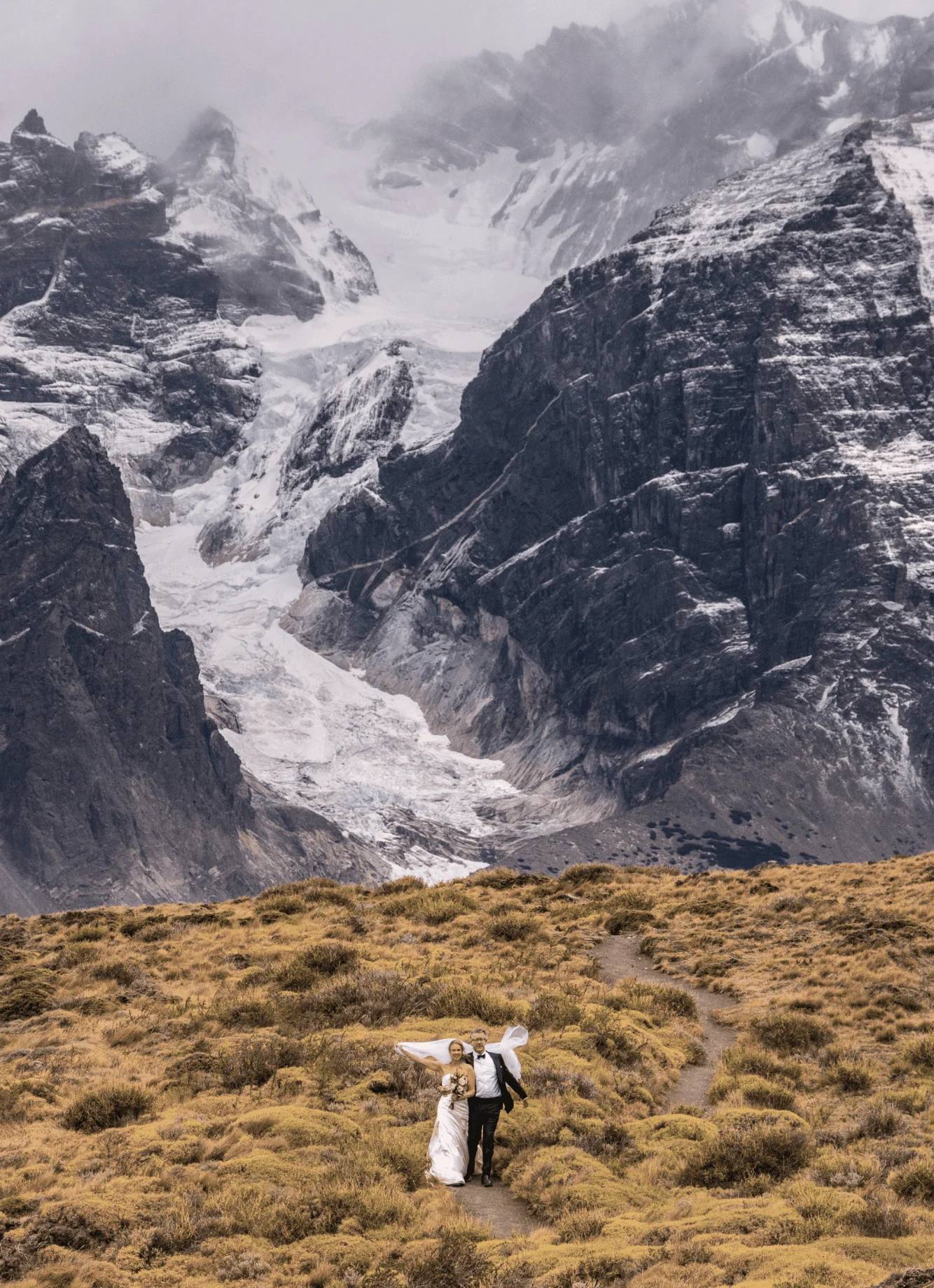 A bride and groom walking a trail below a hanging glacier in Torres del Paine