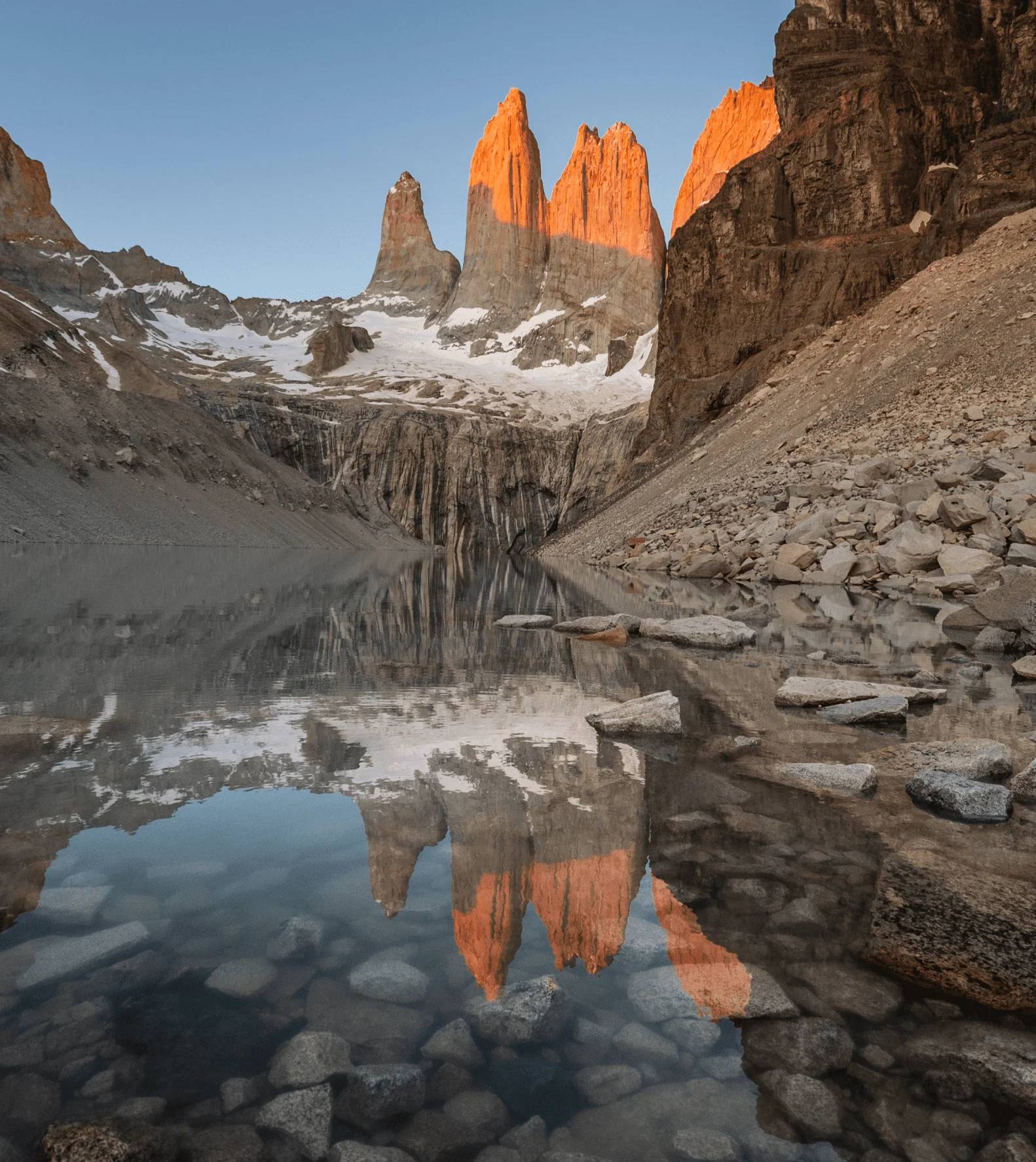 The Torres del Paine towers glowing at sunrise, reflected in the still glacial lagoon below