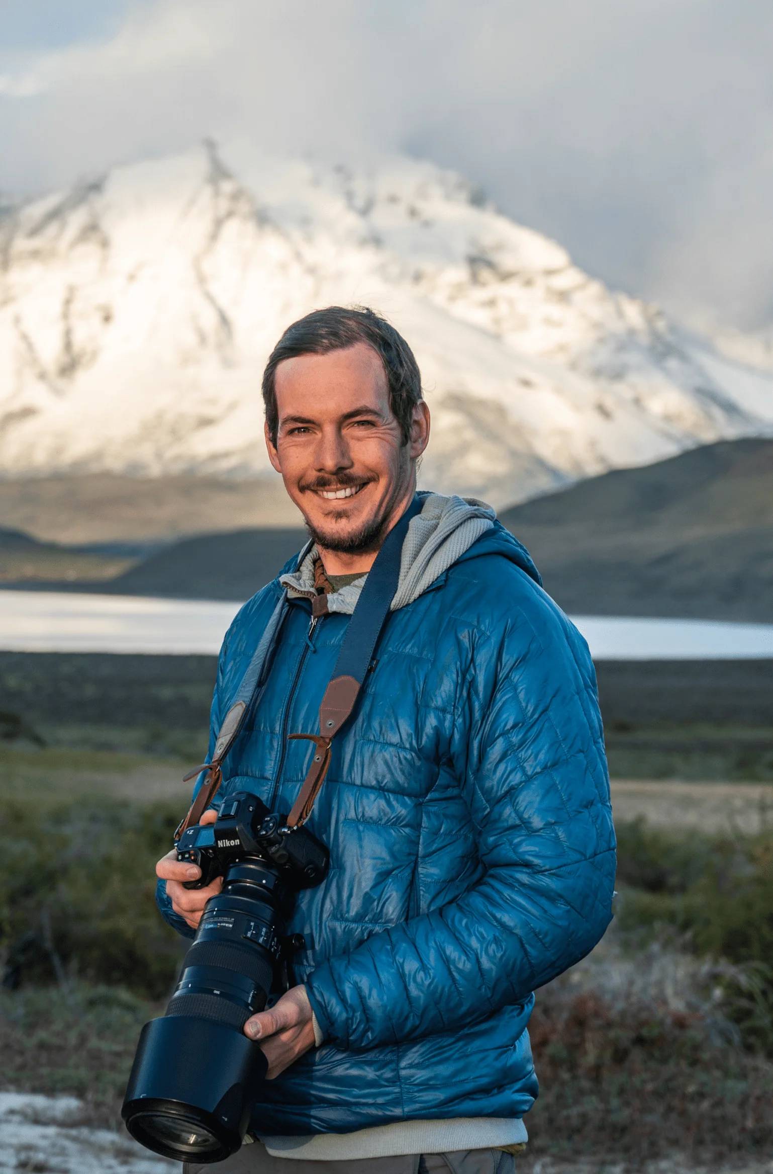 Portrait of Timothy Dhalleine holding his camera, a snow-covered mountain behind him