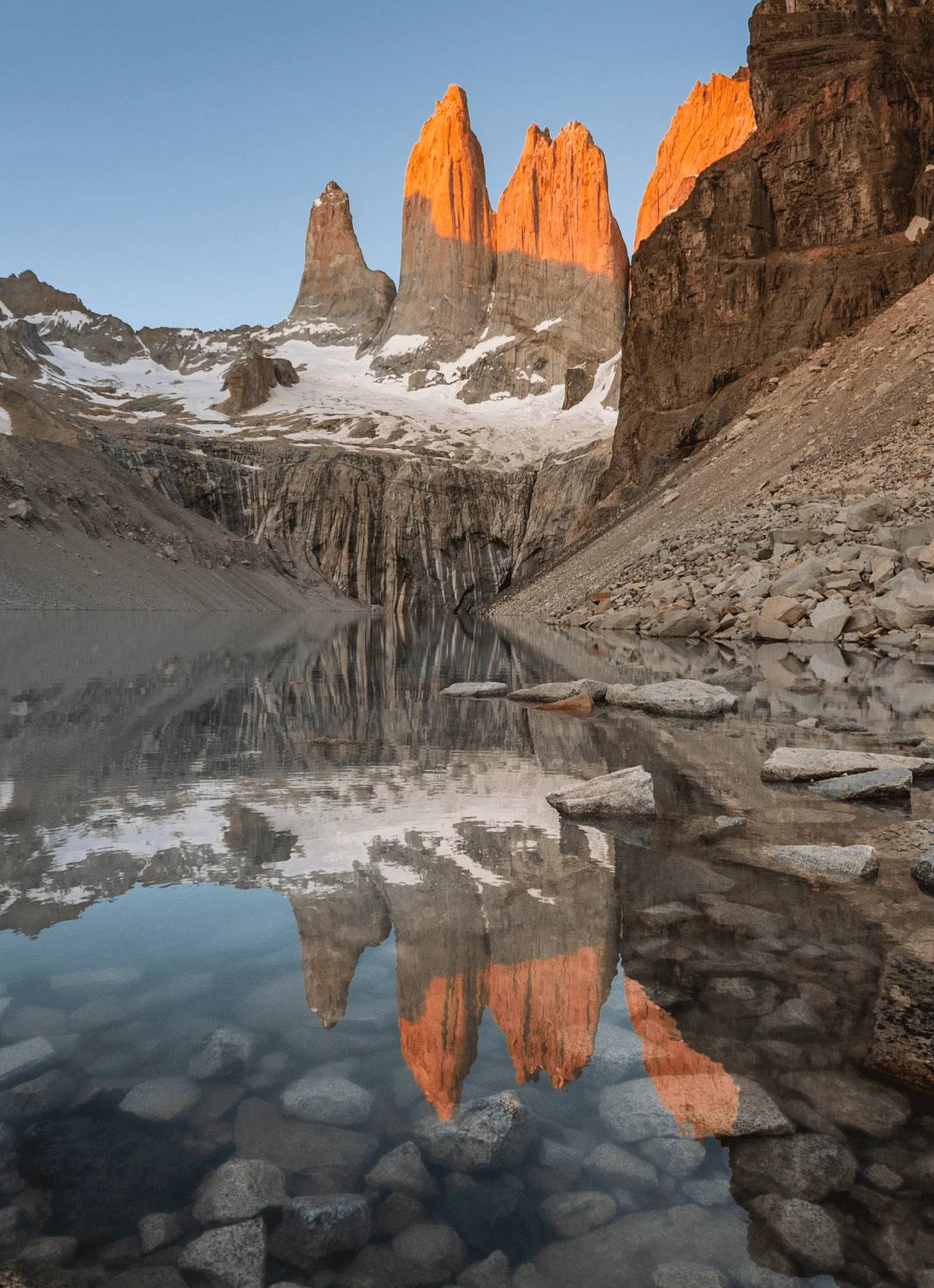 The Torres del Paine granite towers lit orange at sunrise, mirrored in the glacial lagoon at their base