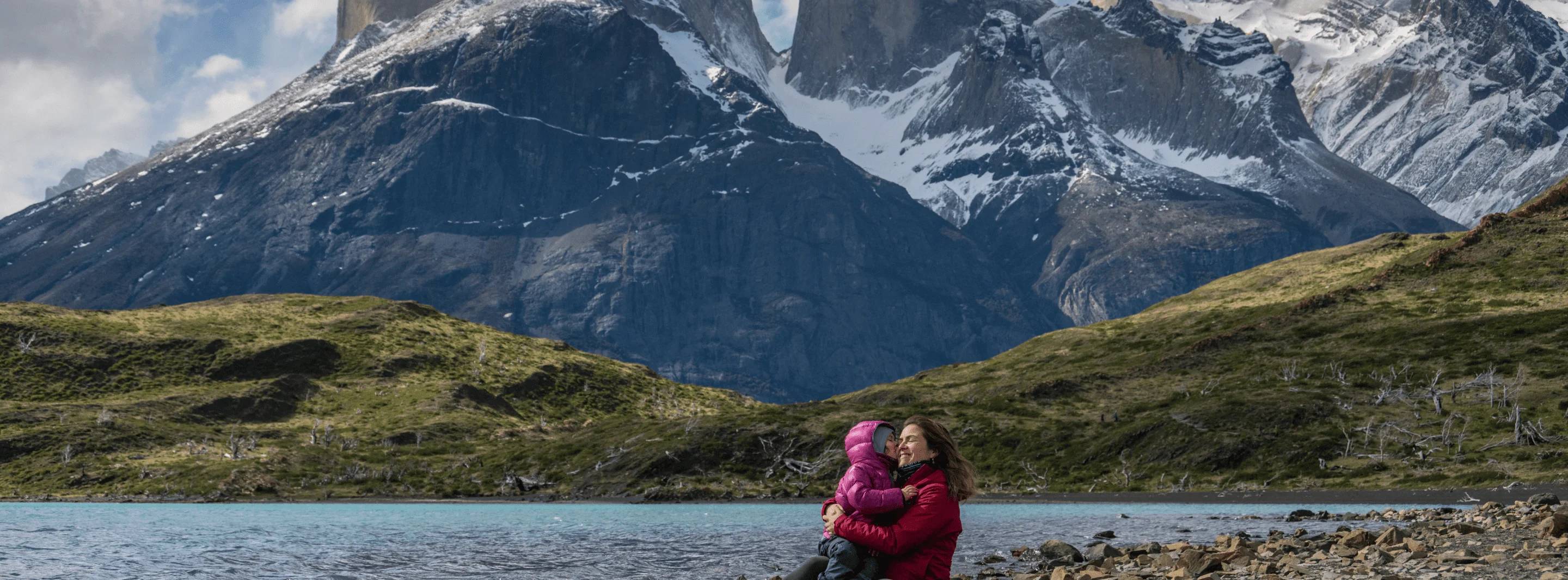 Lisette Nuñez holding their daughter by the lakeshore, the Cuernos del Paine behind them