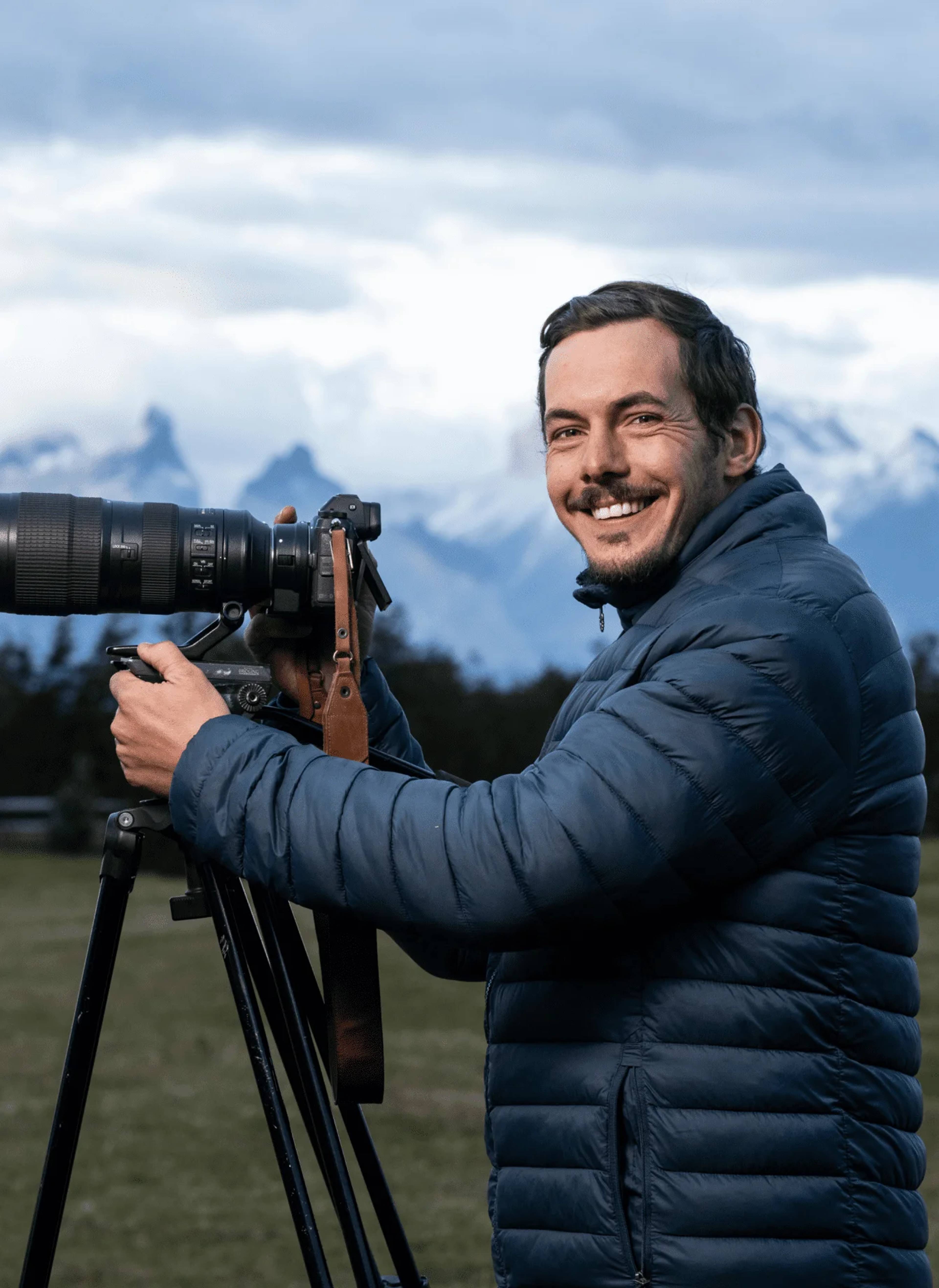 Timothy Dhalleine photographing with a telephoto lens on a tripod, the Cuernos del Paine behind him