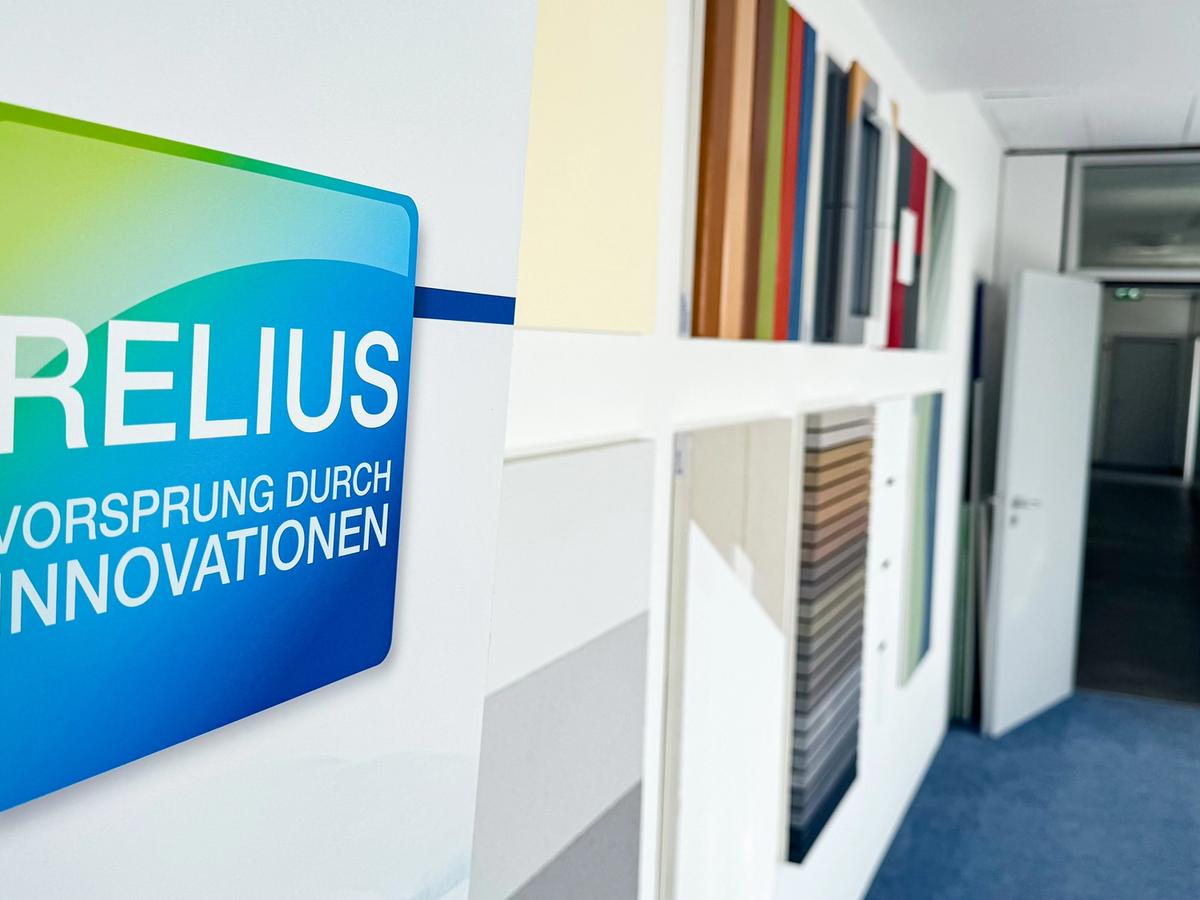 RELIUS-Schild mit dem Schriftzug „Vorsprung durch Innovationen“ in einem Flur mit Farbmustern.