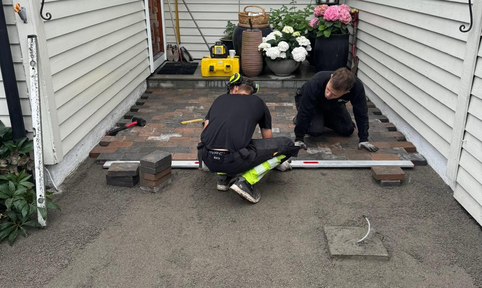 To anleggsgartnere legger heller i en smal passasje mellom hus