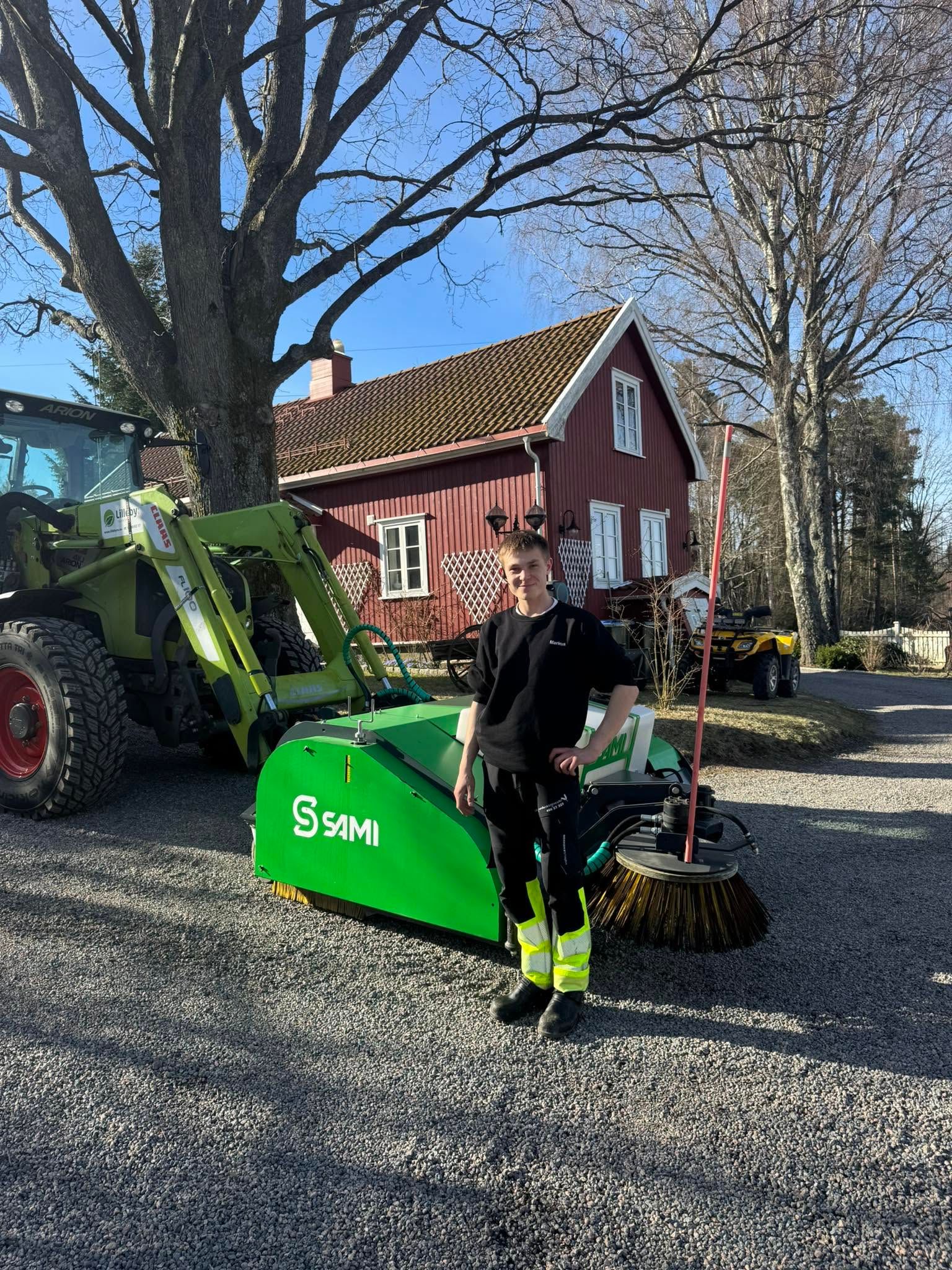 Traktor med feiekost på en grusplass foran et våningshus