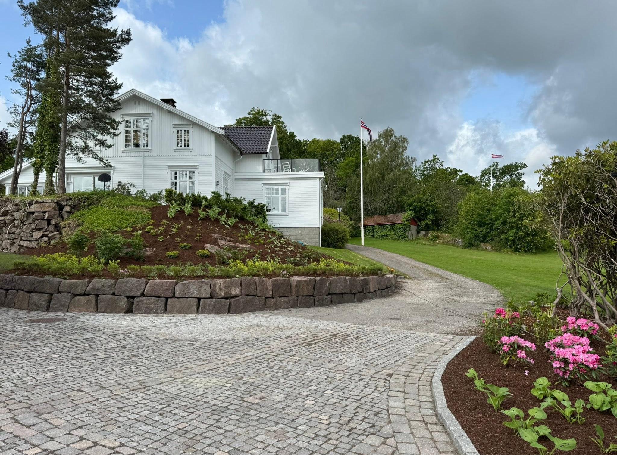 Gårdsplass i smågatestein med natursteinsmur og nytt bed foran et hvitt hus