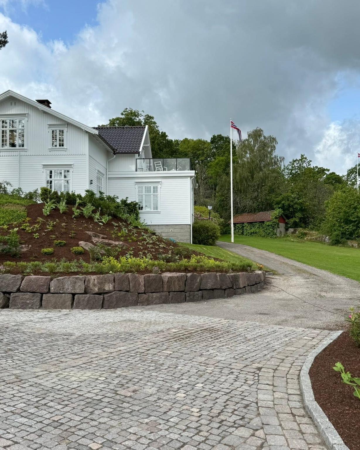 Gårdsplass i smågatestein med natursteinsmur og nytt bed foran et hvitt hus