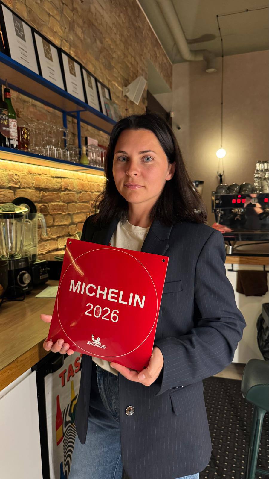 Ludmila Zhilina, Wine Curator of LOWINE, holding the MICHELIN 2026 plaque at the bar