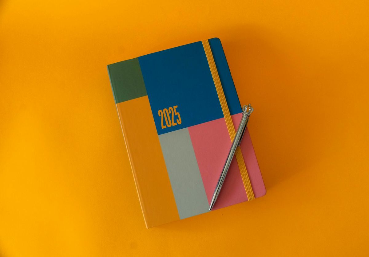 A vibrant 2025 planner with elegant pen on a bold yellow surface, perfect for organizing the year.
