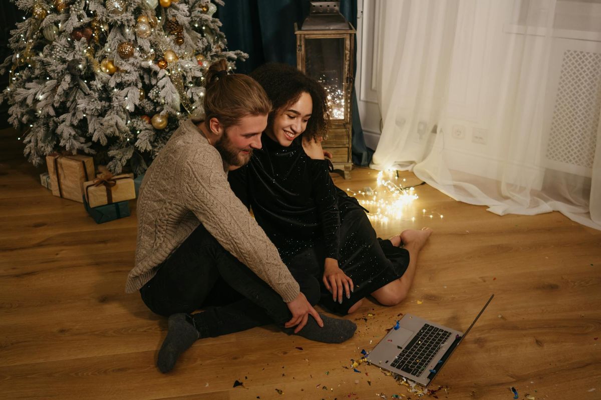 Smiling couple enjoying a Christmas video call by the tree, surrounded by festive decorations and gifts.